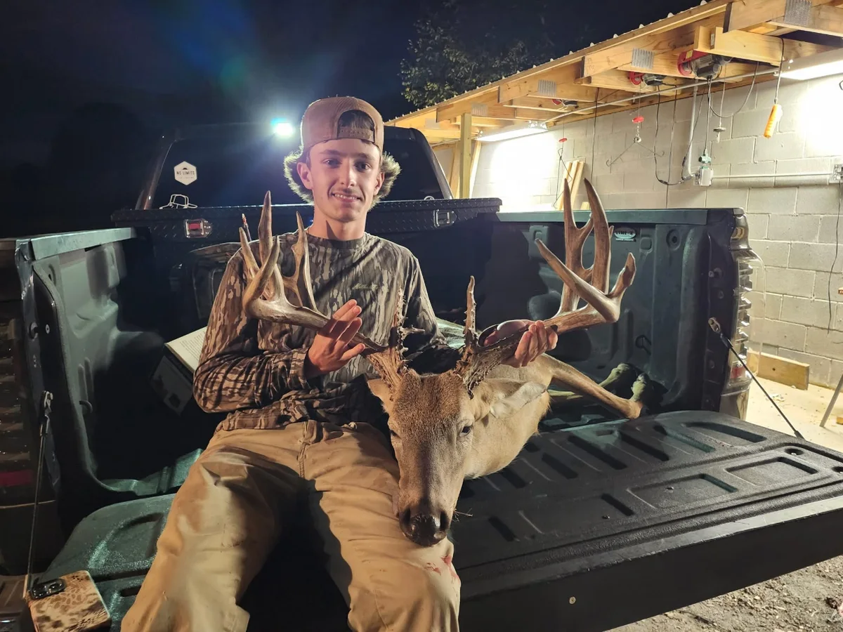 Hunter with a buck in a pickup truck bed outside a building at night.