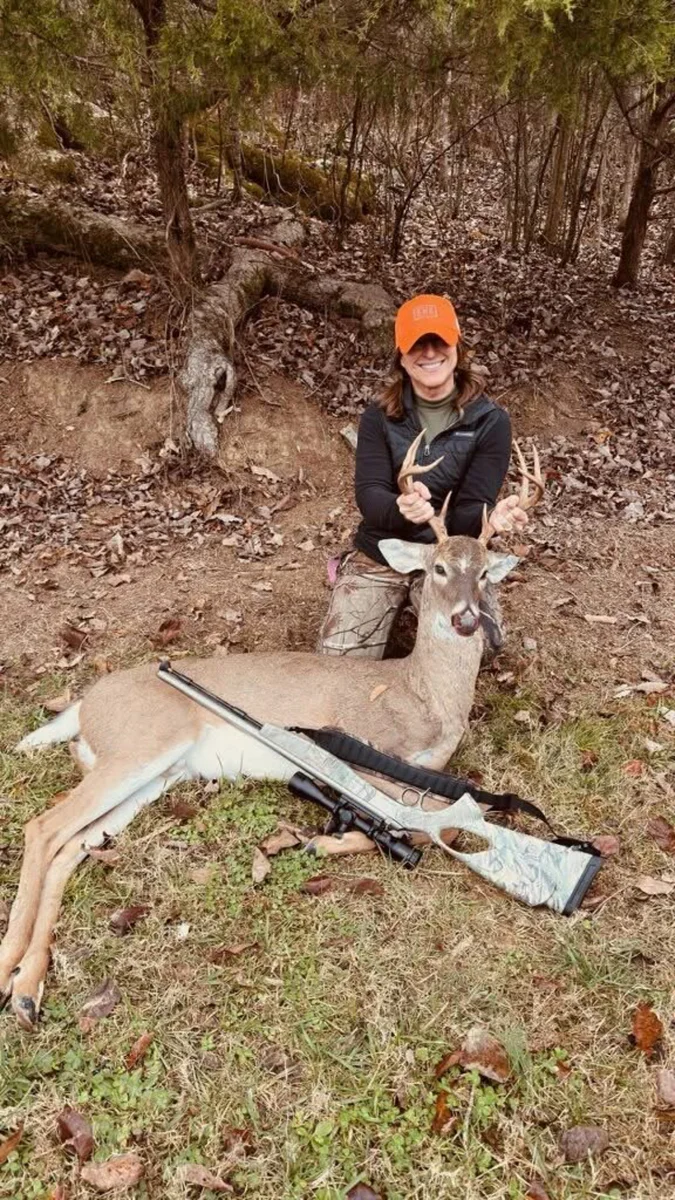 Hunter wearing an orange cap beside a harvested deer in the woods.