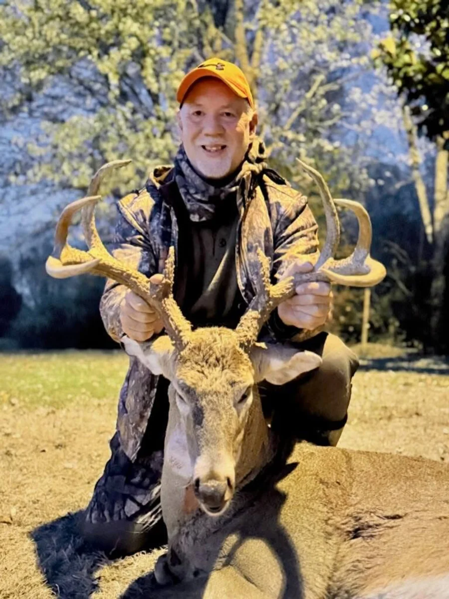 Hunter wearing an orange cap and holding a buck’s antlers.