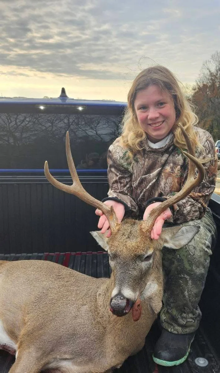 Young hunter holding a buck’s antlers in a pickup truck bed.