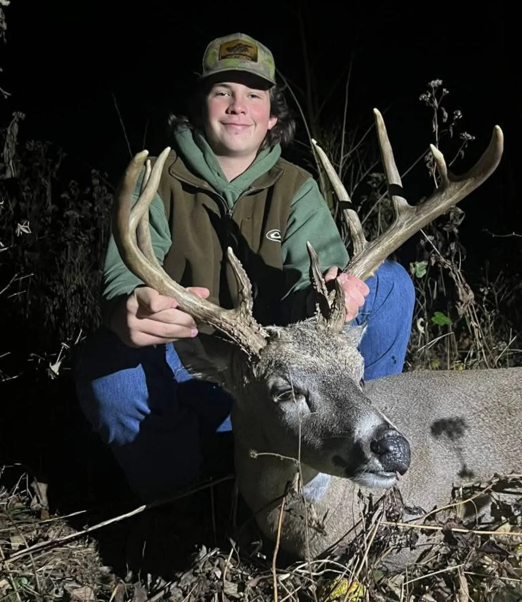 Hunter posing outdoors at night with a harvested buck.