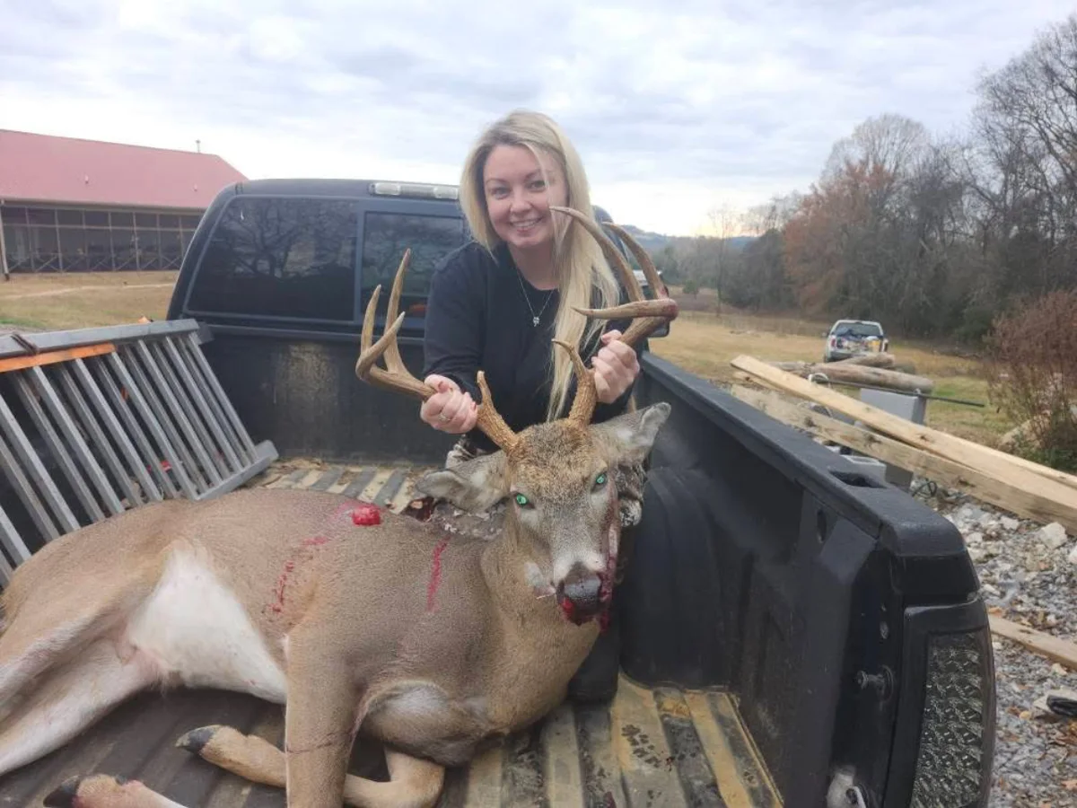 Hunter holding a buck’s antlers in the bed of a pickup truck.